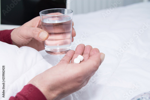 man holding glass of water and looking at pill