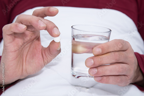 sick man in bed holding a glass of water and pill