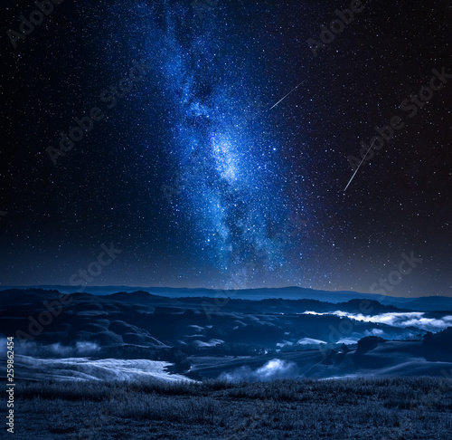 Milky way with falling stars and foggy valley in Italy