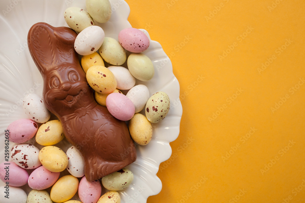 Easter chocolate bunny with colorful eggs on a plate on an orange background .top view copy space Easter chocolate bunny with colorful eggs on a plate on an orange background .top view copy space