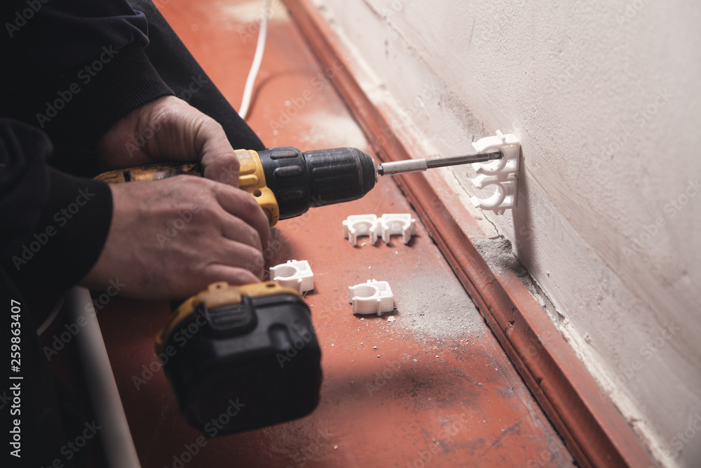 Worker with a cordless screwdriver twists the screw into the wall. Worker with a cordless screwdriver twists the screw into the wall.