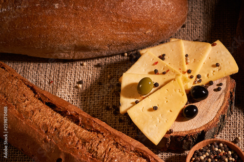 Traditional Dutch semi hard cheese served with olives on rural table with sacking. With baguette and bread