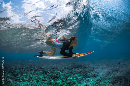 Underwater shot of the young woman surfer diving under the wave with her surfboard