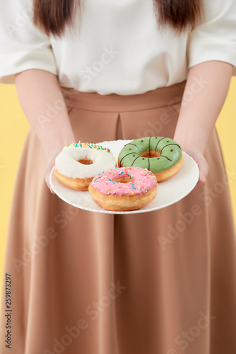 Asian girl show and holding plate full of tasty delicious aromatic donuts in smile face isolated.