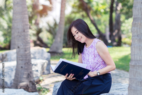 Smile asian woman reading a book in the park with green nature background