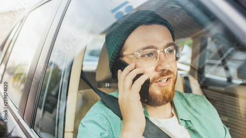 Handsome Young Man Riding on a Passenger Seat of a Car Makes a Phone Call, Talks with Clients, Customers and Business Associates. Camera Shot from Outside the Vehicle.