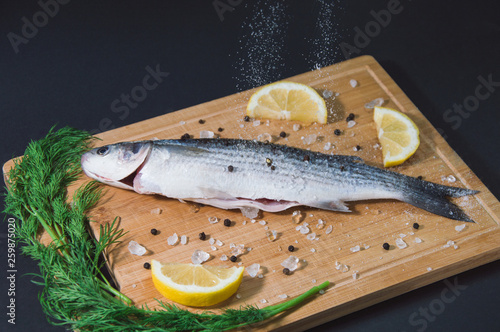 Grey mullet fish on the wooden board wıth lemon, onion and spices.