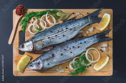 Grey mullet fish on the wooden board wıth lemon, onion and spices.
