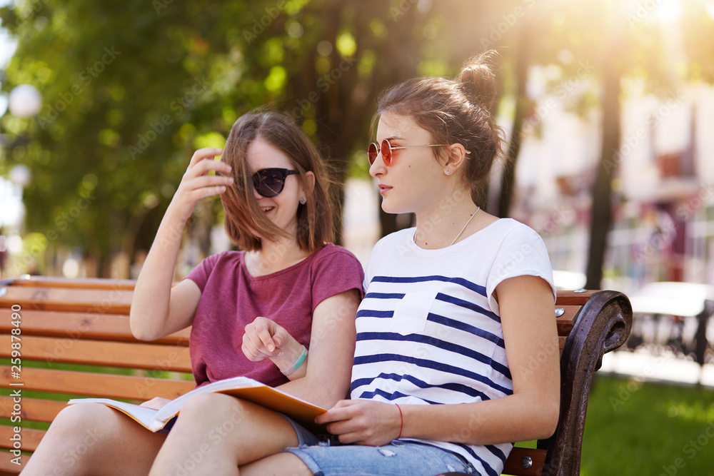 Happy cheerful girls are in the park to enjoy summer atmosphere and read latest news in world. Young beautiful friends give funny comments to each photo and laugh loudly. Friendship concept.