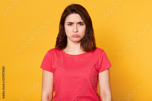 Close up portrait of emotional woman with offended facial expression, crooked lower lip, girl received bad news from husband about weekend, feels disappointed, isolated over yellow background.