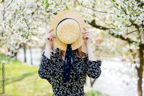 Young girl in a hat stay near a flowering tree