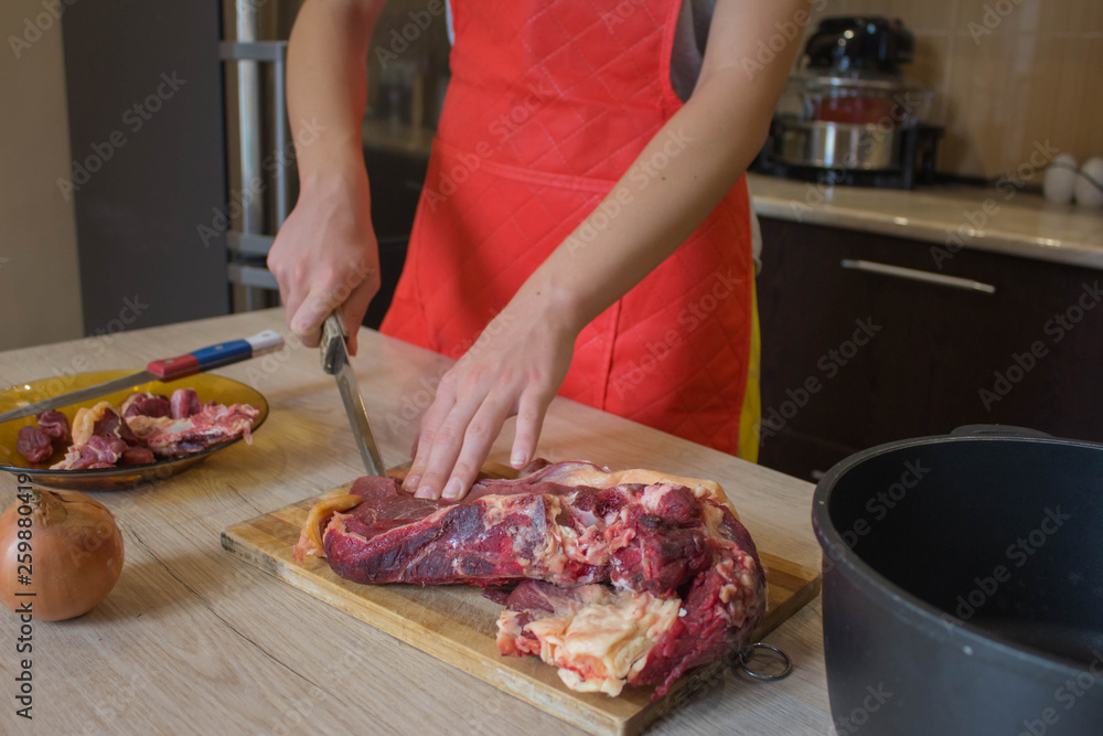 Cook cutting meat on a board and fresh raw vegetables on a table. Food concept