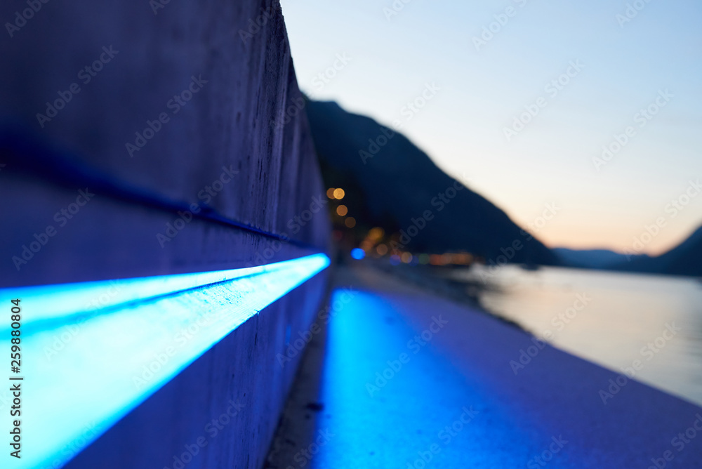 Leuchtender blauer LED-Strahl an einer Mauer in einer abendlichen Alpenlandschaft