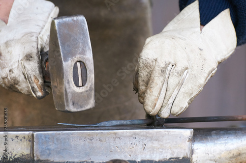 Arbeiter mit weißen Handschuhen schmiedet ein Stück Metall mit einem Hammer auf einem Amboss photo