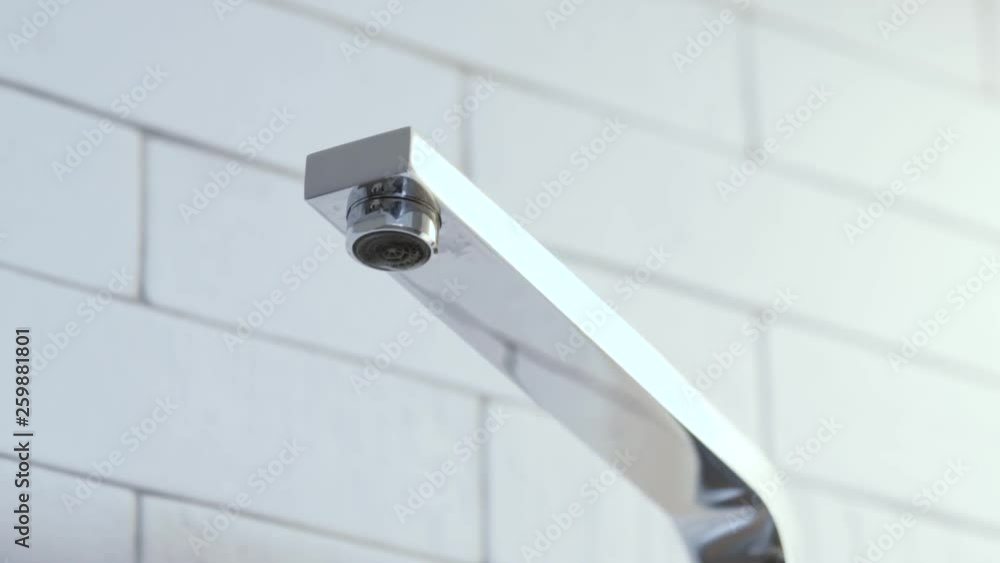 Faucet with dripping water drops on white tile background Faucet with dripping water drops on white tile background