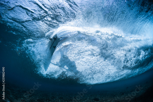 Underwater view of the surfer riding clear ocean wave and making sharp turn