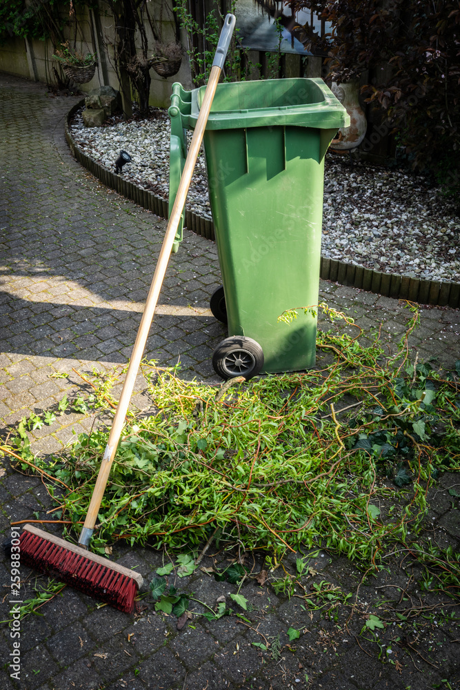 Green wheelie bin / garden waste container and broom filled with fruit