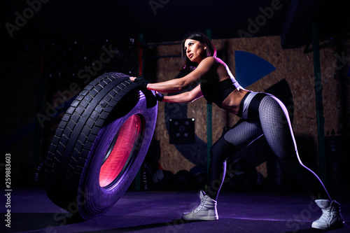 Attractive fit middle age woman athlete working out with a huge tire, turning and flipping in the gym. Crossfit woman exercising with big tire.