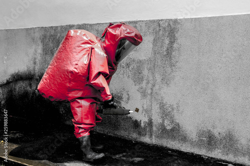 man at work in red hazardous material protective hazmat suit gas mask  rubber gloves and rubber boots checking out a underground train tunnel with geiger counter.