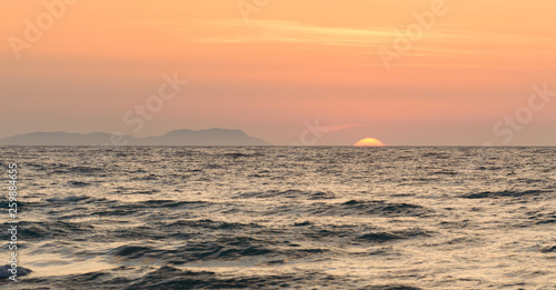 Corfu Sunset over the sea  in the background an island with an orange sun over the water.