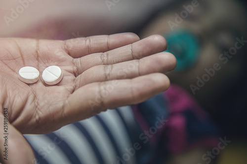 Hand holding medicine pills over Asian kid with pacifier in her mouth.