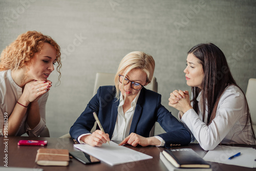 Two female employees with miserable faces asking their blond female boss to arrange a party for the company's Birthday.