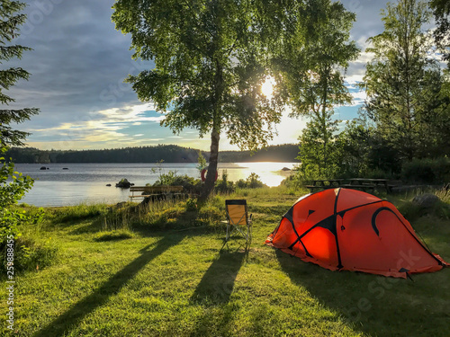 oranges Zelt und Campingstuhl  an einem See, Sonnenuntergang