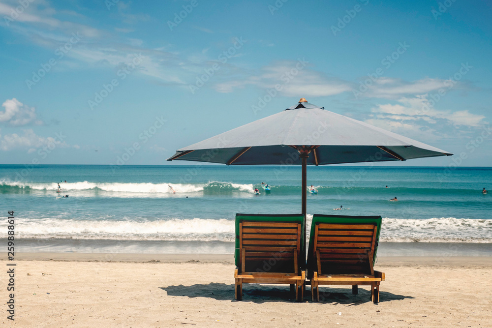 Beach umbrella with deck chairs against the ocean with surfers