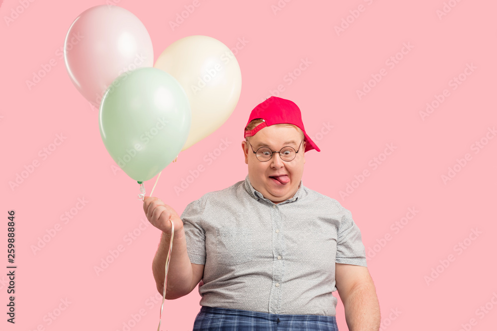 Φωτογραφία Portrait of plump children animator with comic crazy face expression wearing red baseball cap, holding colorful air balloons, looks at camera like a ninny