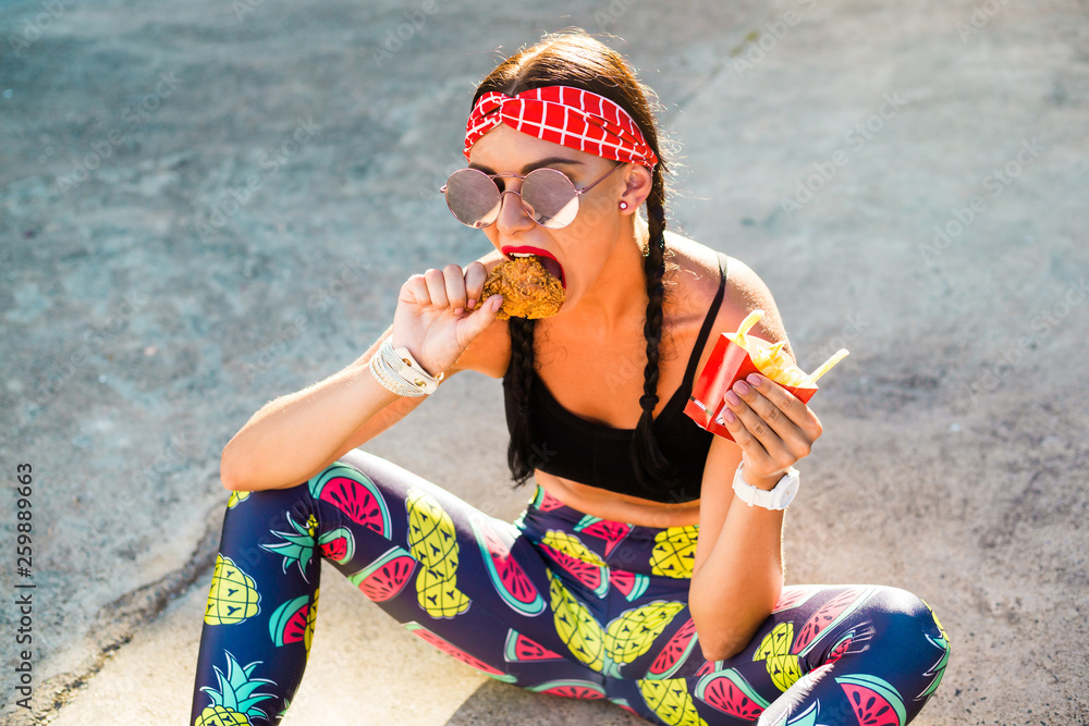 Sports girl in sports clothes, leggings, top, headband, drinks and eats  fast food, 80s 90s style Stock Photo