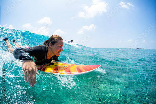 Happy lady surfer paddling and going to take the tropical wave at sunny day