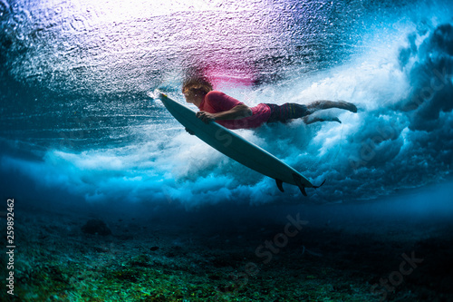 Young male surfer dives under the breaking ocean wave