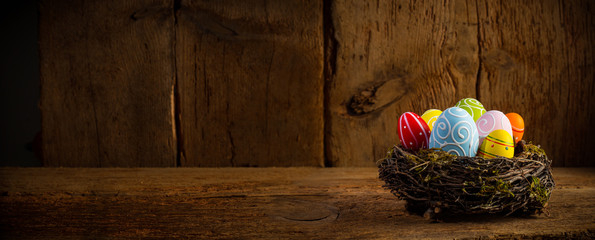 Colorful painted happy easter eggs in birds nest basket on rustic wooden old panorama background copy space