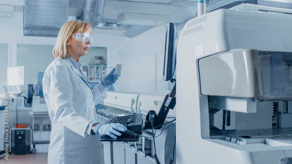 In Laboratory Female Scientist Analyzes Test Tube Data with Blood Samples with Personal Computer. Team of Researchers Work in Pharmaceutical Laboratory. In Laboratory Female Scientist Analyzes Test Tube Data with Blood Samples with Personal Computer. Team of Researchers Work in Pharmaceutical Laboratory.