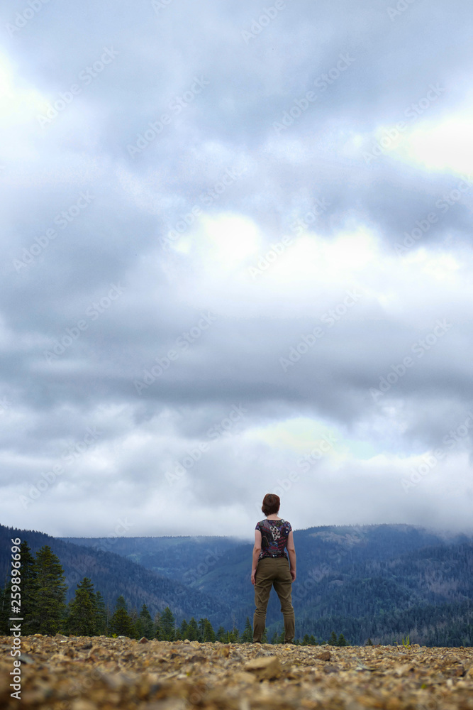 the girl stands with her back against the sky, clouds and hills