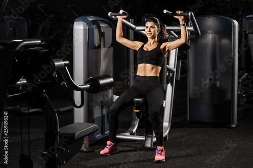 Young fit woman flexing muscles on gym machine. Copy space. Sport, fitness, strength training and people concept.