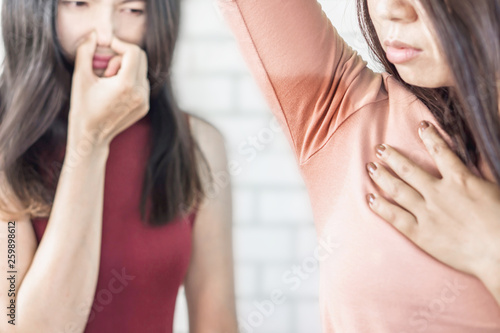 Asian woman having problem sweat under armpit with friend smelling stink in background 