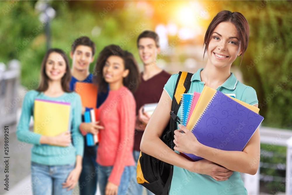 Young girl in Library Holding Notebooks in front of smiling students Young girl in Library Holding Notebooks in front of smiling students