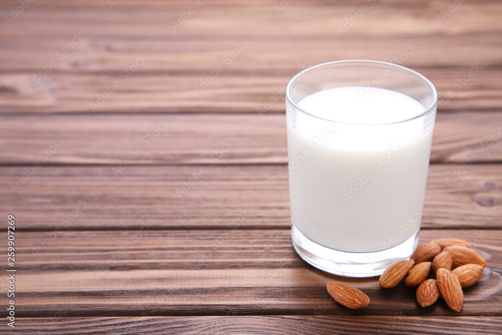 Almond milk in glass with almonds on brown Almond milk in glass with almonds on brown
