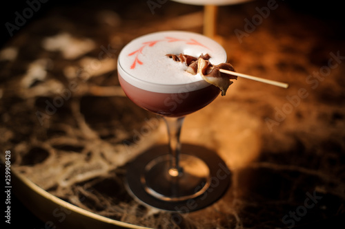 Pink cocktail with a white foam decorated with a bacon on the skewer standing on the marble table