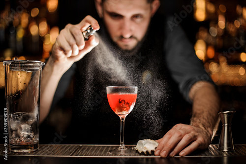 Professional male bartender spraying on the delicious transparent red cocktail in the glass
