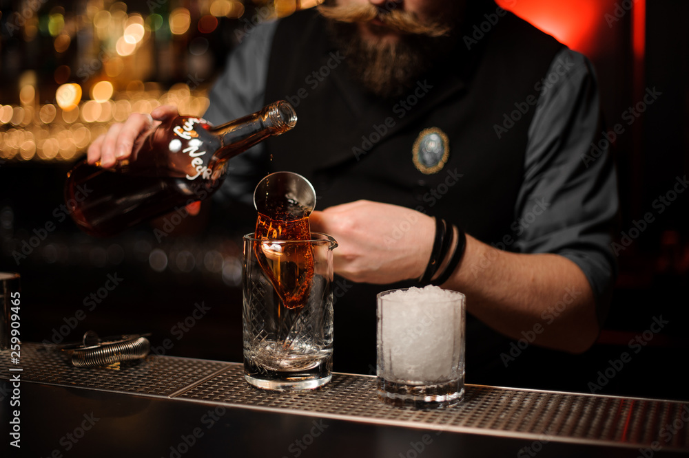 Bartender pouring a delicious brown cocktail from the steel jigger