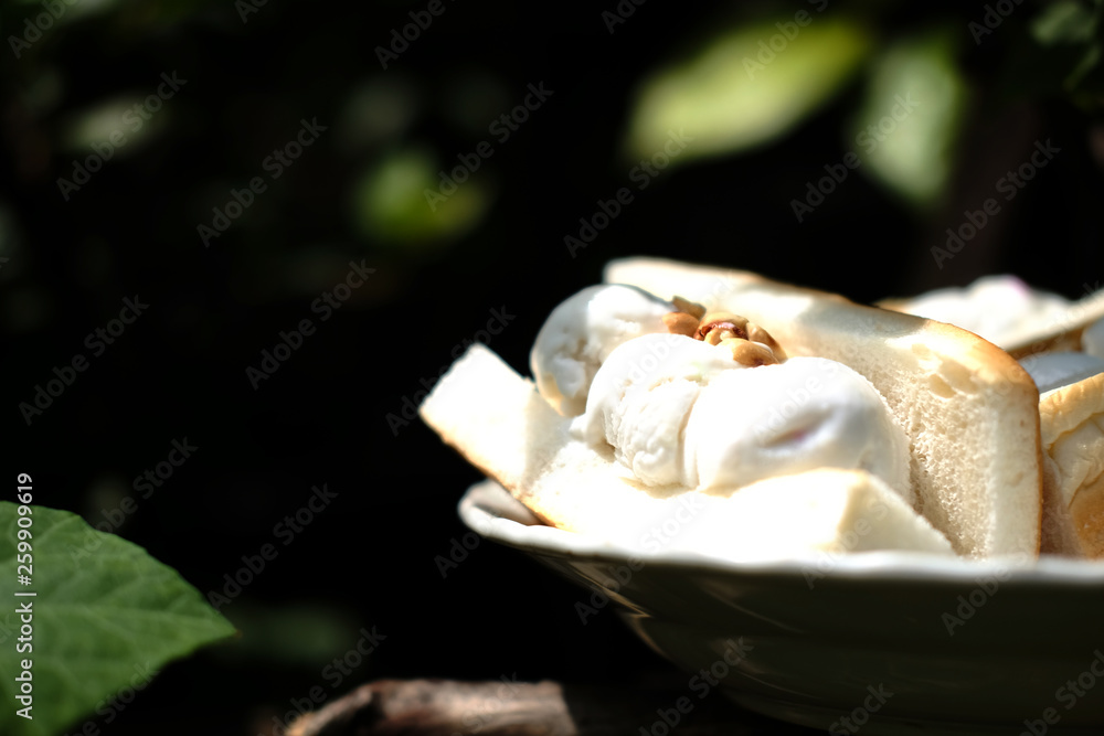 Thai sweet dessert Coconut Ice cream with bread Peanuts Toppings on white dish with sunligh. 