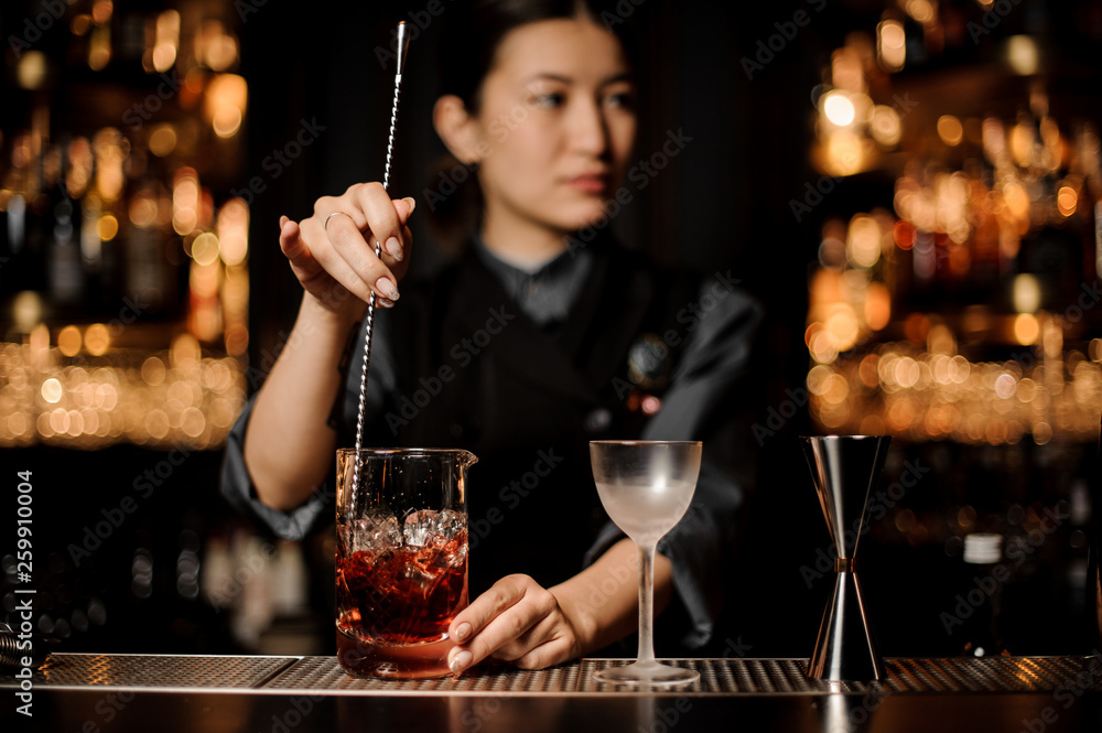 Bartender girl stirring a delicious cocktail with a steel spoon in