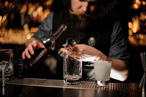 Bartender pouring an alcohol to the cocktail from the steel jigger