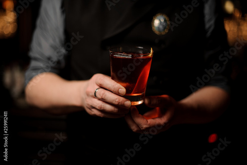 Bartender serving a cocktail in the glass with a orange zest as a decor