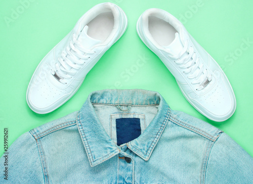 Retro style denim stylish jacket and white hipster sneakers on a mint-colored paper background. Minimalism,80s, top view,flat lay