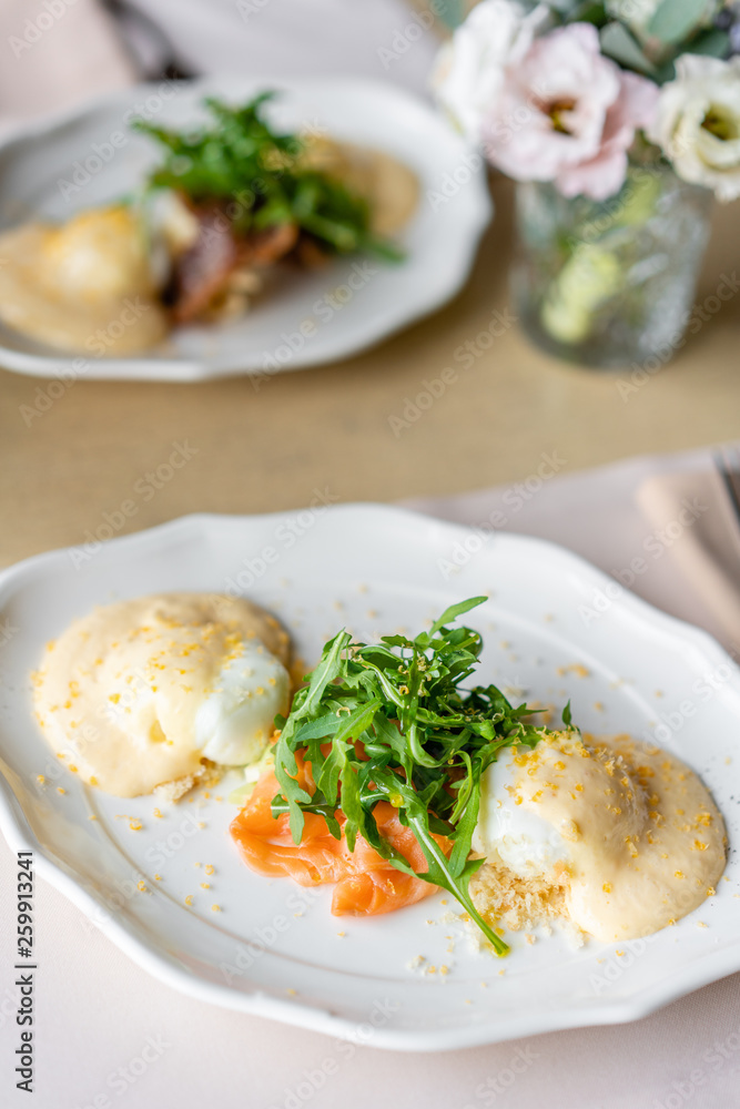 Egg Benedict with little salad on the plate with salmon and arugula. Two eggs delicious hollandaise sauce. Light morning Breakfast on table in restaurant. Egg Benedict with little salad on the plate with salmon and arugula. Two eggs delicious hollandaise sauce. Light morning Breakfast on table in restaurant.