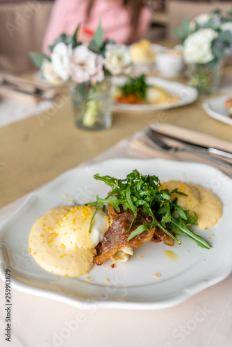 Egg Benedict with little salad on the plate with bacon and arugula. Two eggs delicious hollandaise sauce. Light morning Breakfast on table in restaurant.