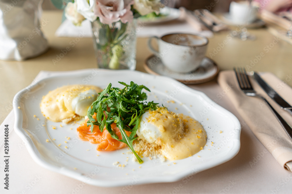 Egg Benedict with little salad on the plate with salmon and arugula. Two eggs delicious hollandaise sauce. Light morning Breakfast on table in restaurant. Egg Benedict with little salad on the plate with salmon and arugula. Two eggs delicious hollandaise sauce. Light morning Breakfast on table in restaurant.